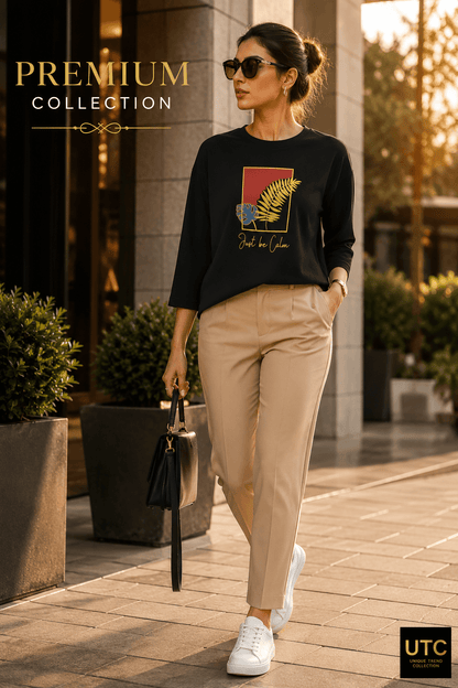 Unique Trend Collection black long-sleeve t-shirt with Just Be Calm botanical graphic worn by a woman with beige pants